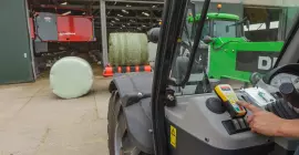 Aktivierung eines Wicklers RW 1110 per Fernsteuerung vor einer Scheune mit Fütterungsroboter im Hintergrund.