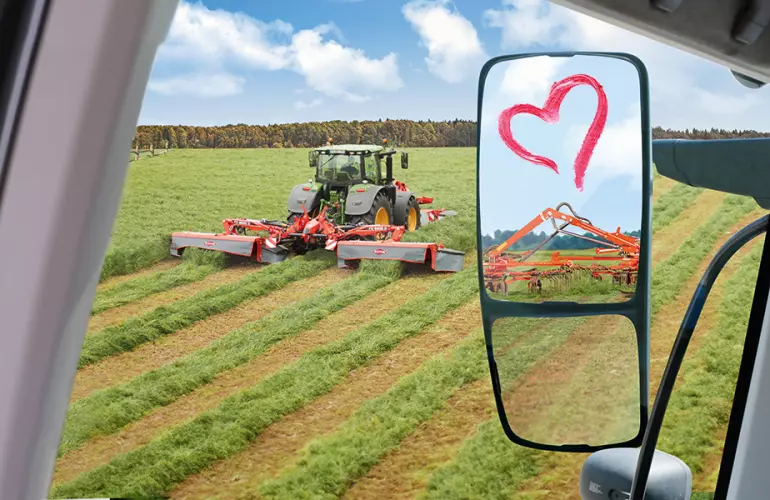 Das Keyvisual für die KUHNaktuell. Herbstrasen 2025, welches den Blick aus einer Traktorkabine auf mehrere Futtererntemaschine der Firma KUHN und ein mit Lippenstift auf den Außenspiegel geschriebenes Herz zeigt