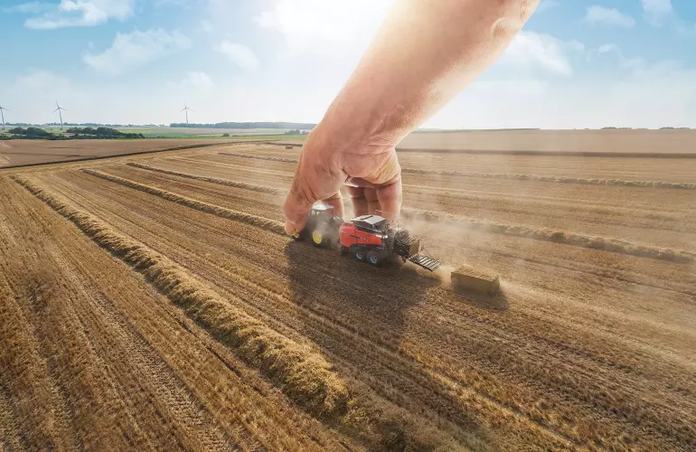 Eine Darstellung der SB 1290 iD, einer Großpackenpresse der Firma KUHN, die wie ein Spielzeug von einem großen Menschen bewegt wird.