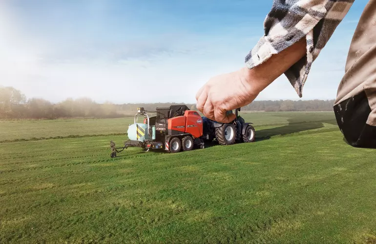 Eine Darstellung der VBP 7190, einer Presswickelkombination der Firma KUHN, die wie ein Spielzeug von einem großen Menschen bewegt wird.