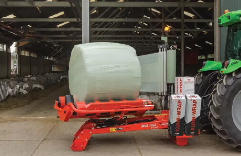 RW 1110 beim Wickeln eines Rundballens vor einer Ziegenscheune.