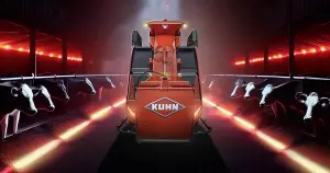 Die autonome Fütterungsmaschine AURA von KUHN im Scheinwerferlicht in einem dunklen Kuhstall mit Kühen rechts und links und roter Neon-Beleuchtung