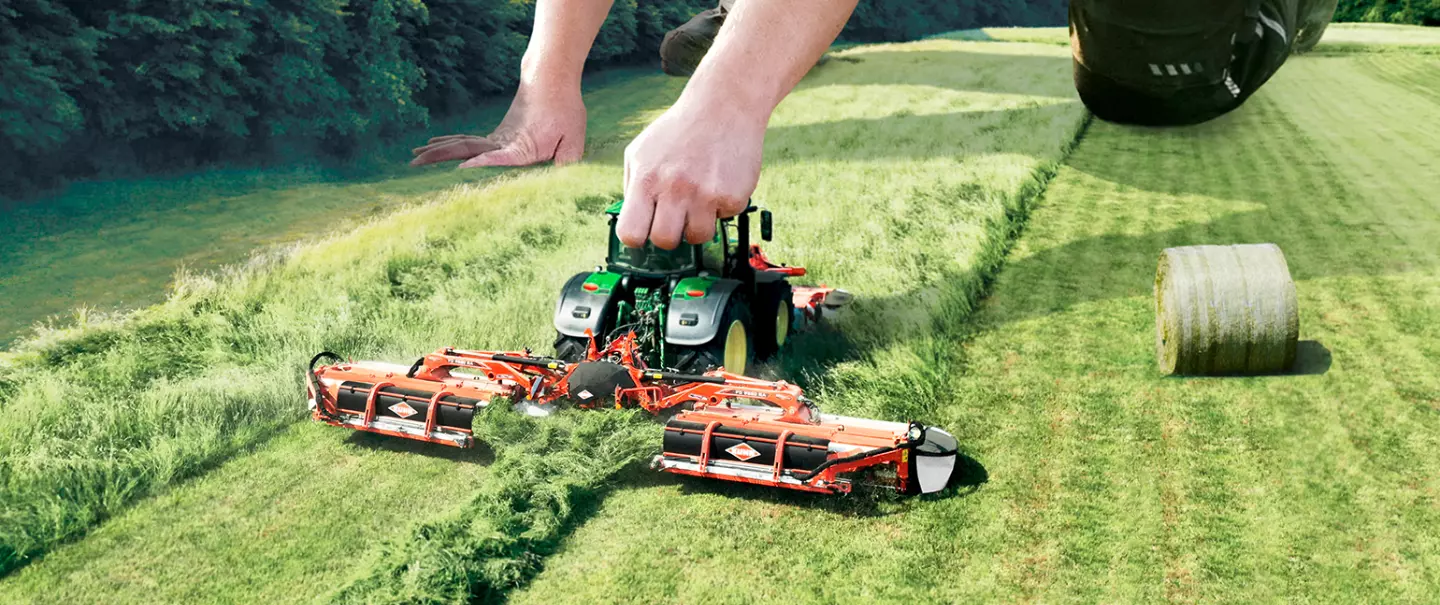 Eine Darstellung des FC 9330 RA, einer Dreifach-Scheiben-Mähknickzetter-Kombination der Firma KUHN, die wie ein Spielzeug von einem großen Menschen bewegt wird.