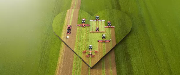Das Keyvisual der KUHNaktuell. Herbstrasen 2026, welches KUHN Futtererntemaschinen in einem Herz auf dem Feld darstellt.