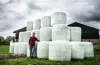 Photo illustrant un agriculteur devant un stock de balles rondes enrubannées.